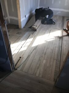 A worker installing hardwood flooring planks in a room, showcasing a handyman job by Franco's Hardwood Flooring in Durham, NC.