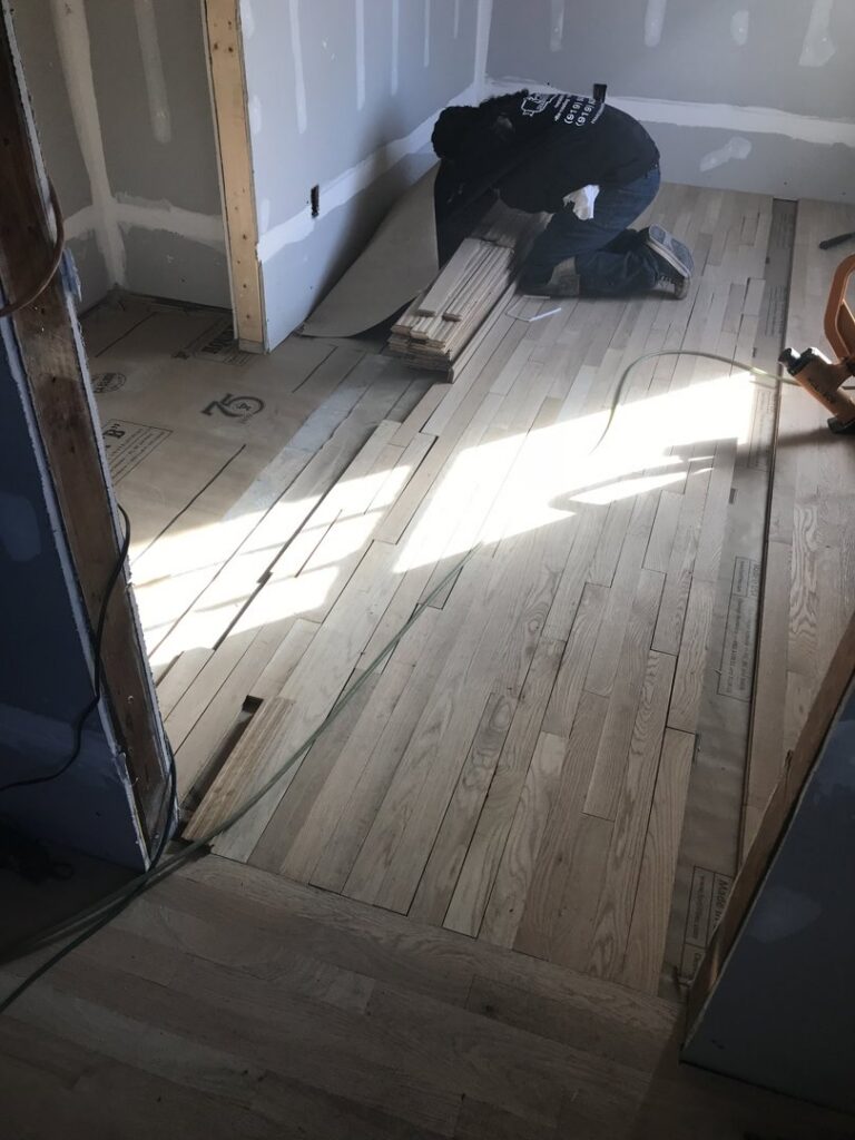 A worker installing hardwood flooring planks in a room, showcasing a handyman job by Franco's Hardwood Flooring in Durham, NC.