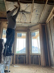 A worker on stilts installing insulation or ceiling material in a framed room by Metro Insulation in Rockford, IL.