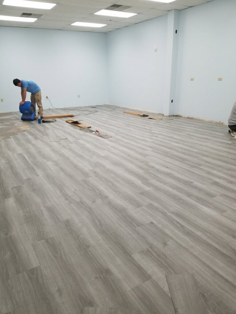 A worker installing laminate plank flooring in a commercial space by JMQ Contractor INC in Philadelphia, PA