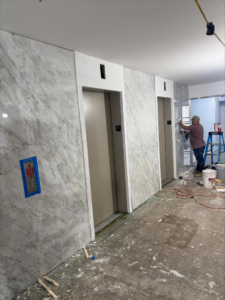 A worker installing wall panels near elevator doors in a hallway by Golden Tile Construction in Yonkers, NY.