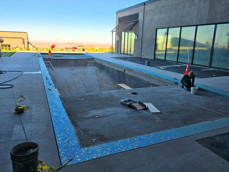 A worker installing blue mosaic tiles along the edge of a pool for Premier Paradise, Inc. in Gilbert, AZ.