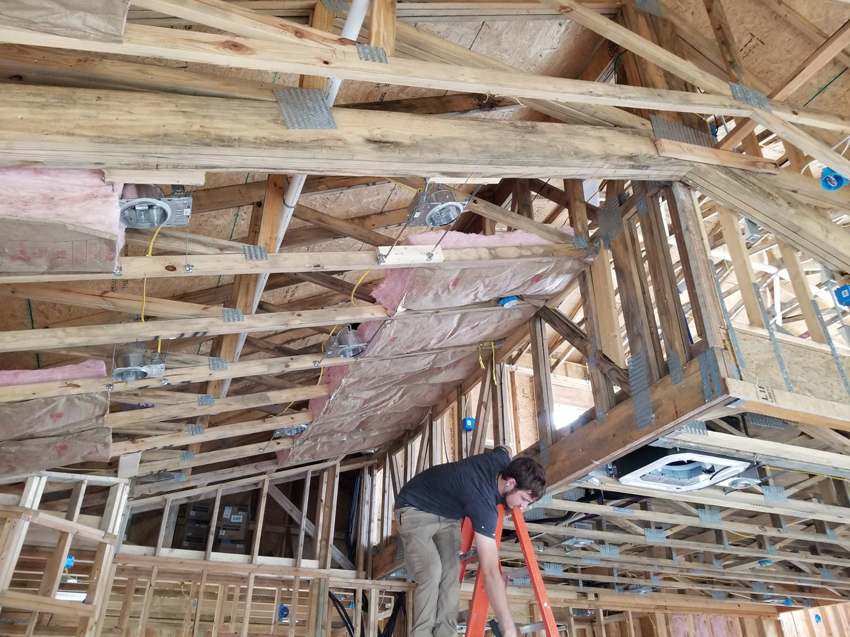 A worker on a ladder installing recessed lighting and wiring in a home by Blown Rite Insulation and Gutters in Wilmington, NC.