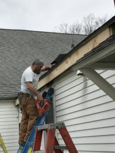 A worker on a ladder installing or repairing a roof and gutter section on a house, performed by Advanced Seamless Gutters, Inc. in Chicopee, MA.