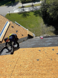 A worker in a safety harness installing roof underlayment on a plywood deck for New American General Construction INC in Richmond, VA.