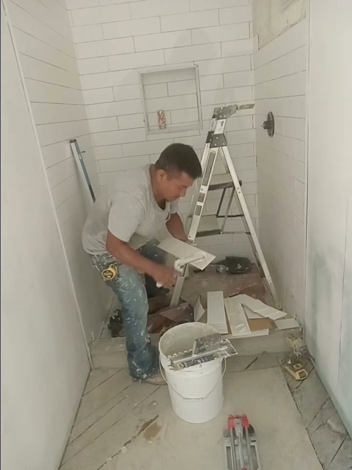 A worker installing white subway tiles in a shower during a bathroom renovation by Juancho's Handyman in Salida, CO.