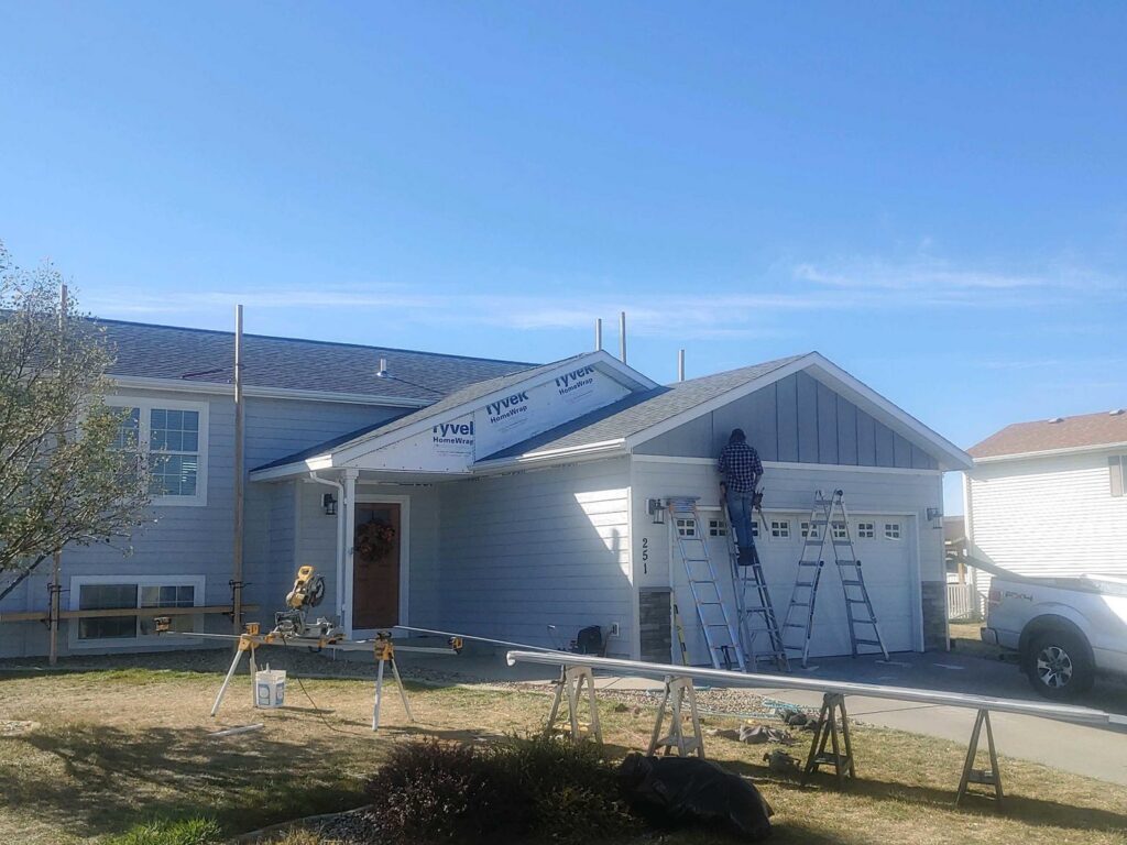 A worker on a ladder installing siding on the front of a house, showcasing a renovation project by Rapid Renovations LLC in Rapid City, SD.