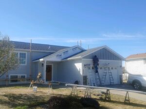 A worker on a ladder installing siding on the front of a house, showcasing a renovation project by Rapid Renovations LLC in Rapid City, SD.