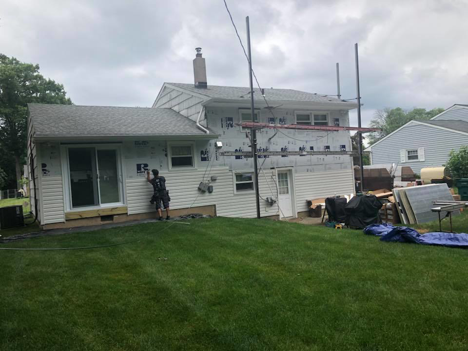 A worker installing new siding on a house, with scaffolding and construction materials visible, by Quality Care Home Improvements in Hamilton, NJ.