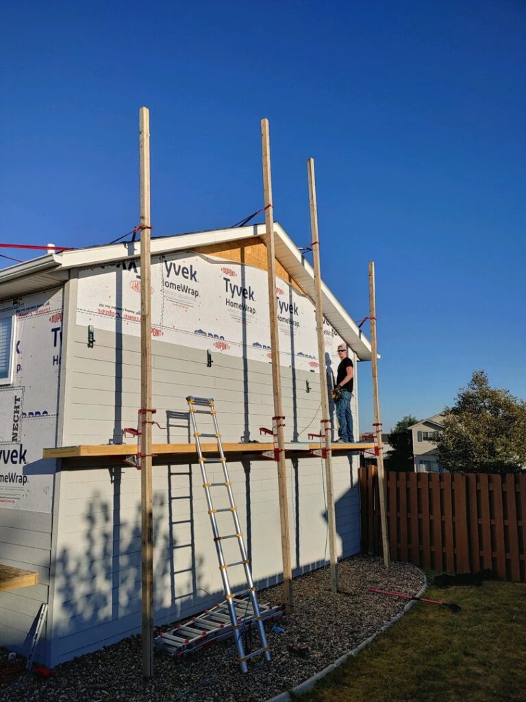 A worker on scaffolding installing new siding on the exterior of a house, demonstrating a handyman job by Rapid Renovations LLC in Rapid City, SD.