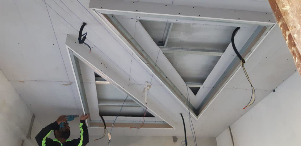 A worker installing unique triangular-shaped ceiling drywall with exposed wiring for TechPro Constructions in Houston, TX.