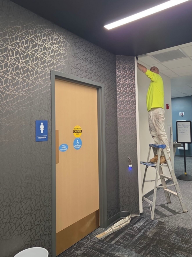 A handyman from Blair Commercial Painting LLC installing wall covering or performing trim work in a commercial restroom in Waukesha, WI.