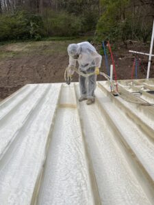 A worker applying spray foam insulation to floor joists on a construction site by Spray Foam Art-Insulation in Stamford, CT.