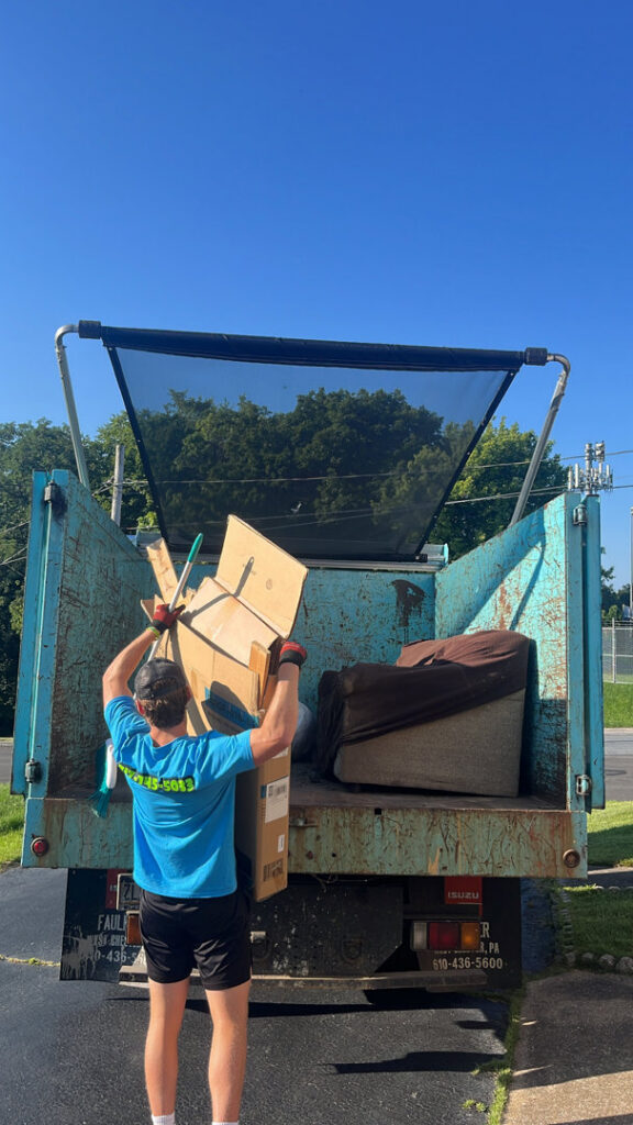 A worker loading a cardboard box into a junk removal truck for You Call We Haul Junk Removal in Milwaukee, WI.