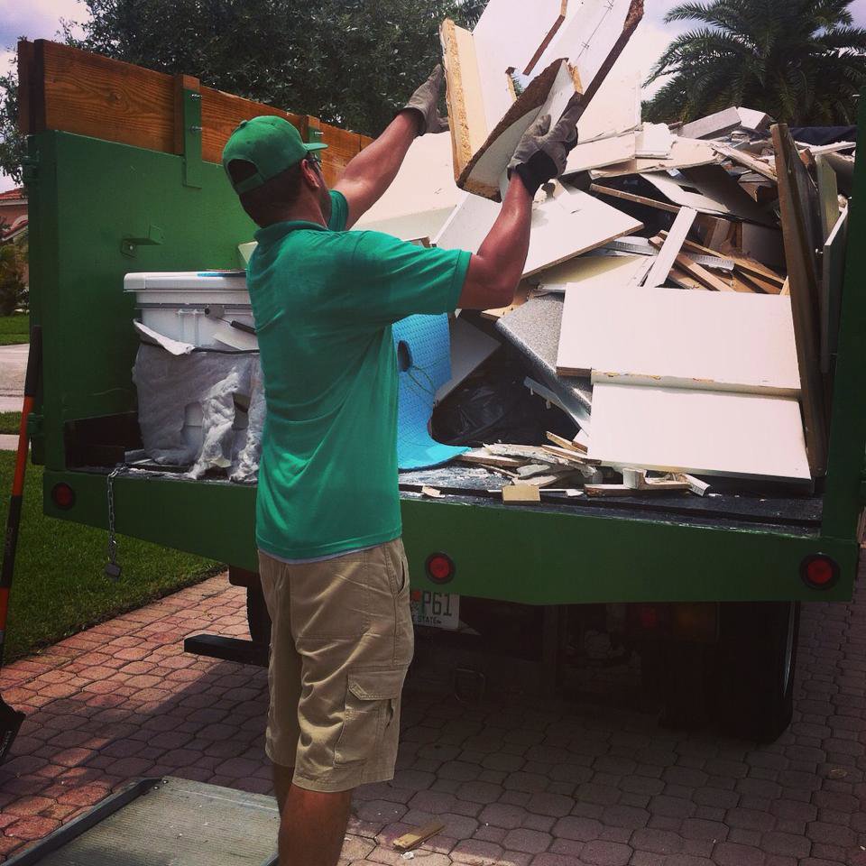A Gator Junk Removal worker loading wood and construction debris into a dump truck in Miami, FL.