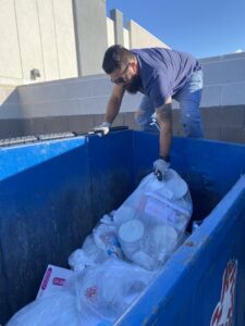 A worker climbs onto a dump trailer to load or arrange junk, performing a junk removal job for Mike's Dumper in Las Vegas, NV.