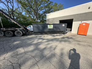 A worker operating a roll-off truck to load a dumpster at a job site for Premier Recycling and Disposal in Waukesha, WI.