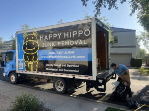 A worker loading bags of junk onto a Happy Hippo Junk Removal truck in Scottsdale, AZ.