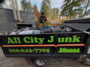 A worker loading junk into an All City Junk Removal branded truck, filled with trash bags and debris, performing a job in Kent, WA.