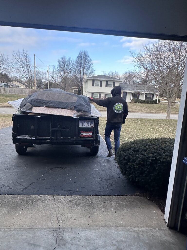 A 614junkremoval team member standing next to a trailer loaded with junk covered by a tarp in Columbus, OH.