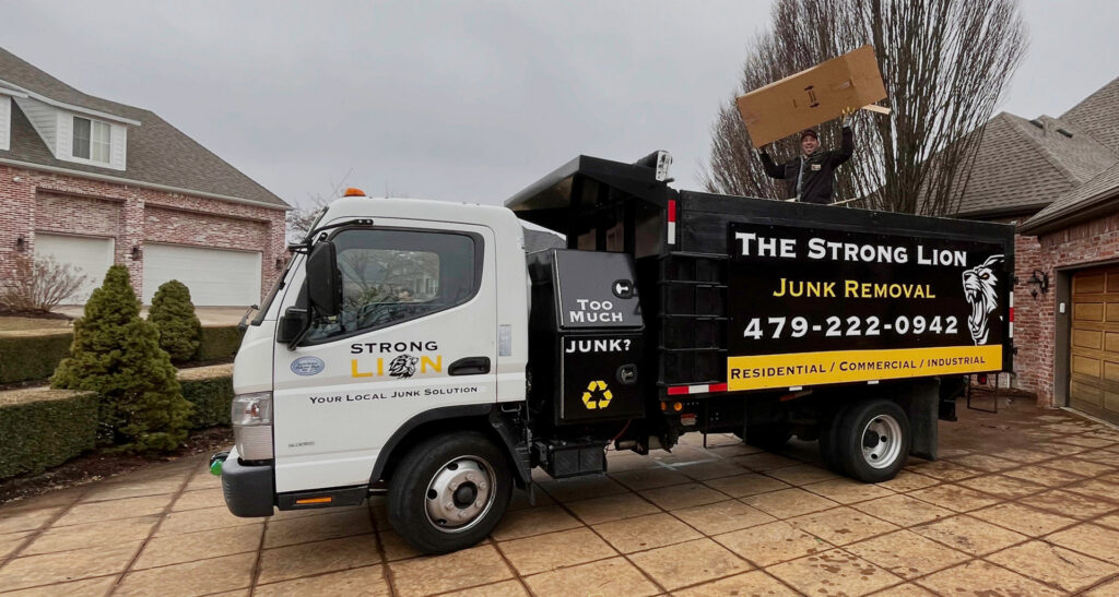 A Strong Lion Junk Removal worker loading a box onto the back of a junk removal truck in Fayetteville, AR.