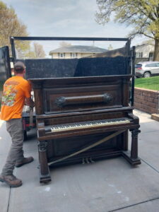 A worker loading a heavy, old piano onto a junk removal truck, showcasing services by Omaha Junk Removal in Papillion, NE