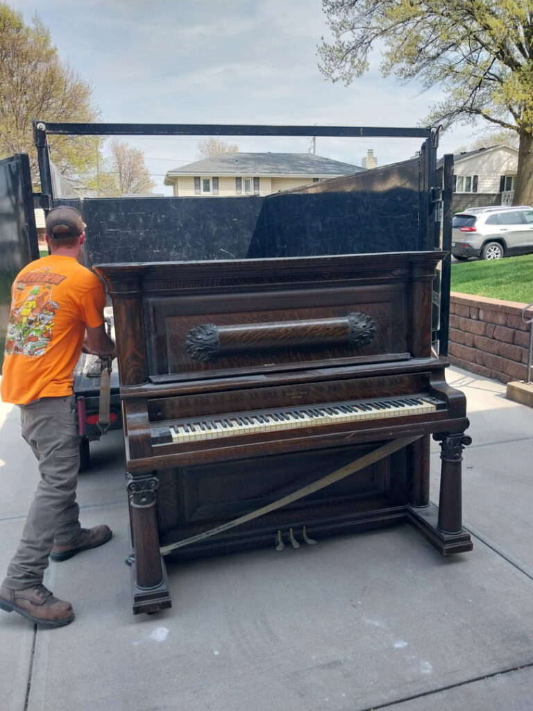 A worker loading a heavy, old piano onto a junk removal truck, showcasing services by Omaha Junk Removal in Papillion, NE
