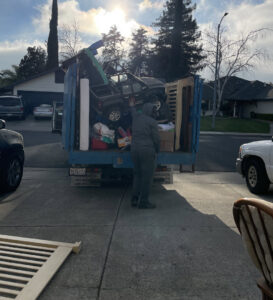 A worker loading a large toy truck and other items into a Junk Away & Cleaning truck in Sacramento, CA.