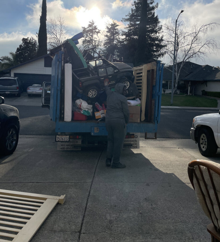 A worker loading a large toy truck and other items into a Junk Away & Cleaning truck in Sacramento, CA.