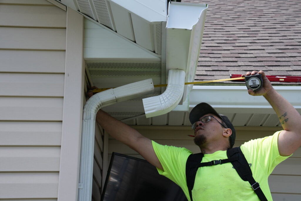 A Helitech Waterproofing & Foundation Repair worker measuring a gutter system on a house in Kingdom City, MO.