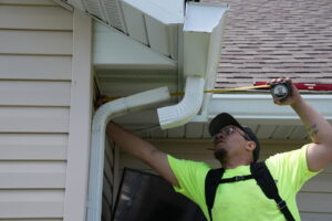 A Helitech Waterproofing & Foundation Repair worker measuring a gutter system on a house in Kingdom City, MO.