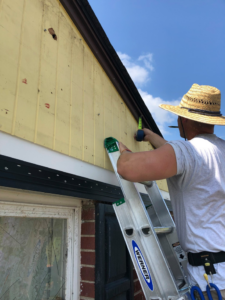 A worker on a ladder measuring siding on a house, performing a handyman job for Recover Roofing in Dayton, OH.