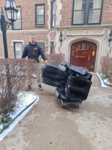 A worker moving an old black recliner on a dolly for In & Out Junk Removal Service LLC in Chicago, IL.