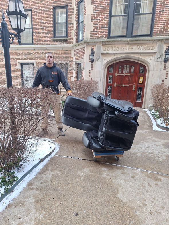 A worker moving an old black recliner on a dolly for In & Out Junk Removal Service LLC in Chicago, IL.