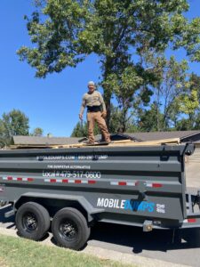 A worker standing on a Mobiledumps dumpster trailer filled with construction debris during a junk removal job in Rogers, AR.