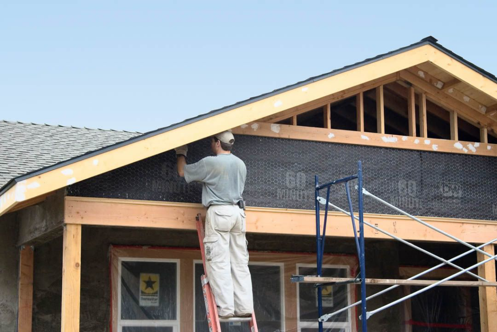 A worker on a ladder applying exterior material to a house, representing construction and repair services by World General Construction LLC in Everett, WA.