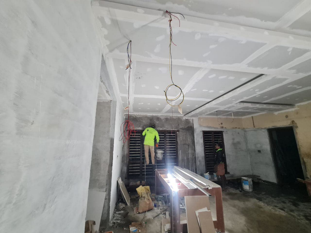 A worker on a ladder in a room with newly installed ceiling and wall drywall, showcasing progress by TechPro Constructions in Houston, TX.