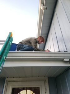 A worker on a ladder carefully painting or sealing the fascia of a house, demonstrating exterior work by Drew's Handy Construction in Charleston, IL.