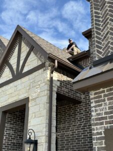 A Riker Home Services worker on a roof performing gutter repair or installation in Plano, TX