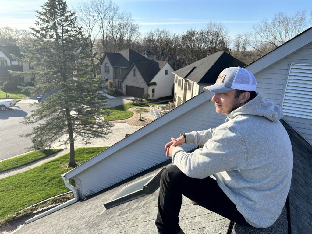 A SHIFT Roofing & Exteriors worker sitting on a residential roof, possibly inspecting, in Gahanna, OH