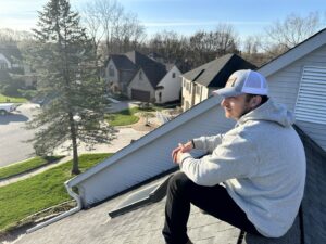 A SHIFT Roofing & Exteriors worker sitting on a residential roof, possibly inspecting, in Gahanna, OH