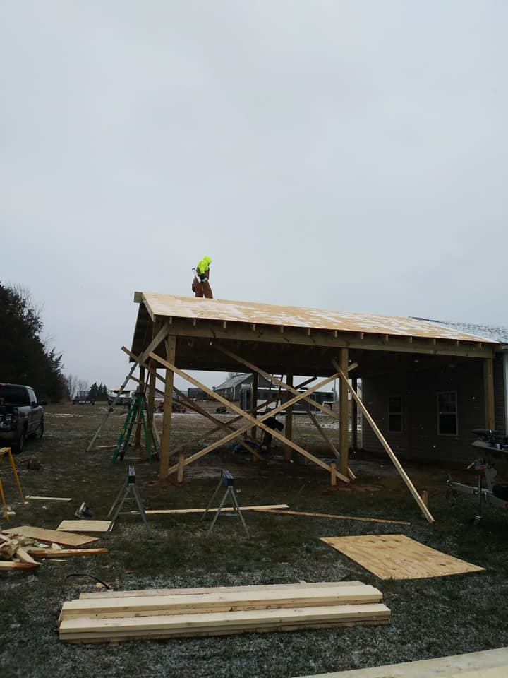 A worker on the roof of a wooden carport structure during construction, performed by Any Length Improvements in Bowling Green, KY.