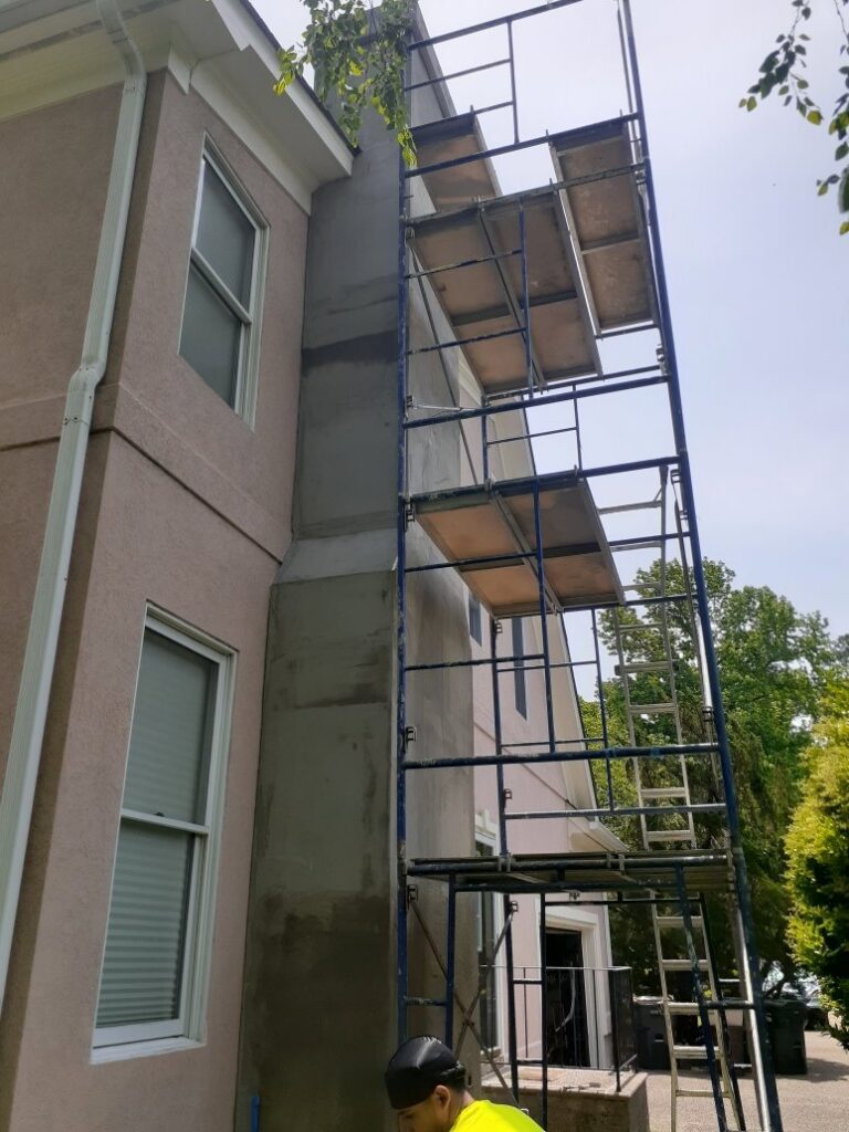 A worker on scaffolding applying stucco or EIFS to the exterior of a house by Modern Wall Systems in Virginia Beach, VA.