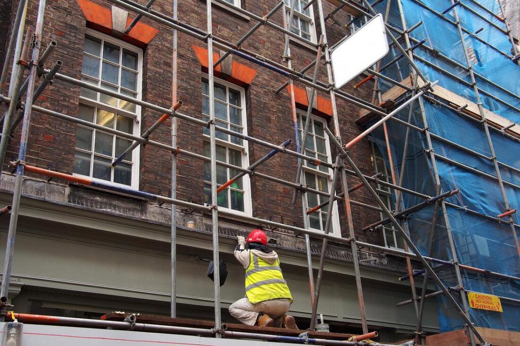 A worker on scaffolding performing exterior repair on a brick building, a service by Foundation Repair and Waterproofing in Philadelphia, PA.