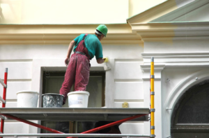 A worker on scaffolding painting the exterior trim of a building, demonstrating exterior painting services by World General Construction LLC in Everett, WA.