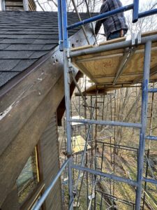 A worker on scaffolding repairing the siding and roofline of a house by Cedar Siding Repair in Centerville, OH.