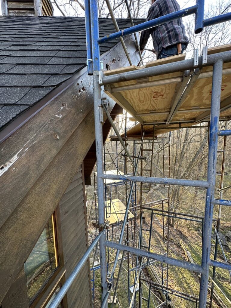 A worker on scaffolding repairing the siding and roofline of a house by Cedar Siding Repair in Centerville, OH.