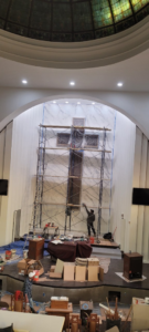 A worker on scaffolding repairing a wall with a large stained glass cross at a job site by Modern Wall Systems in Virginia Beach, VA.