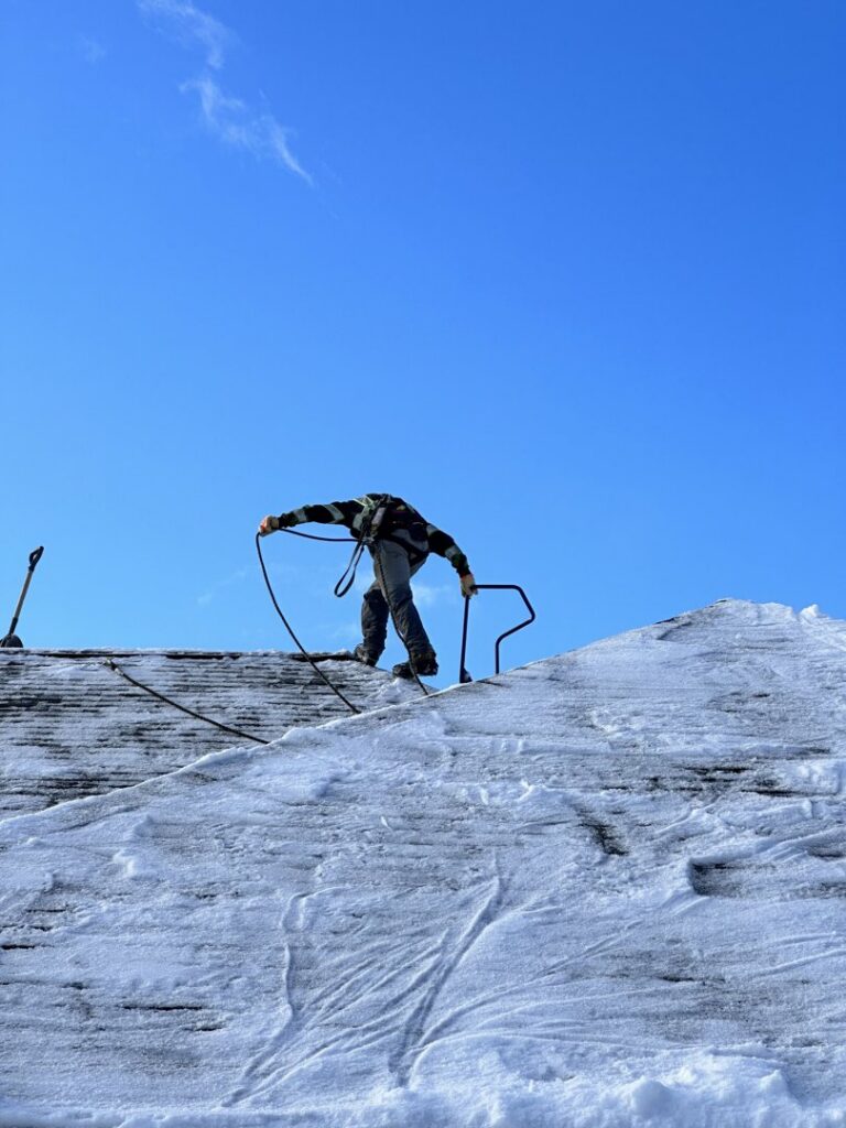 A worker on a snowy roof preparing for or performing snow removal services for Alaskan Residential Rescue in Anchorage, AK.
