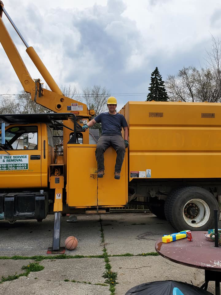 A worker sitting on a yellow tree service truck from JT Tree Service & Removal in Toledo, OH.